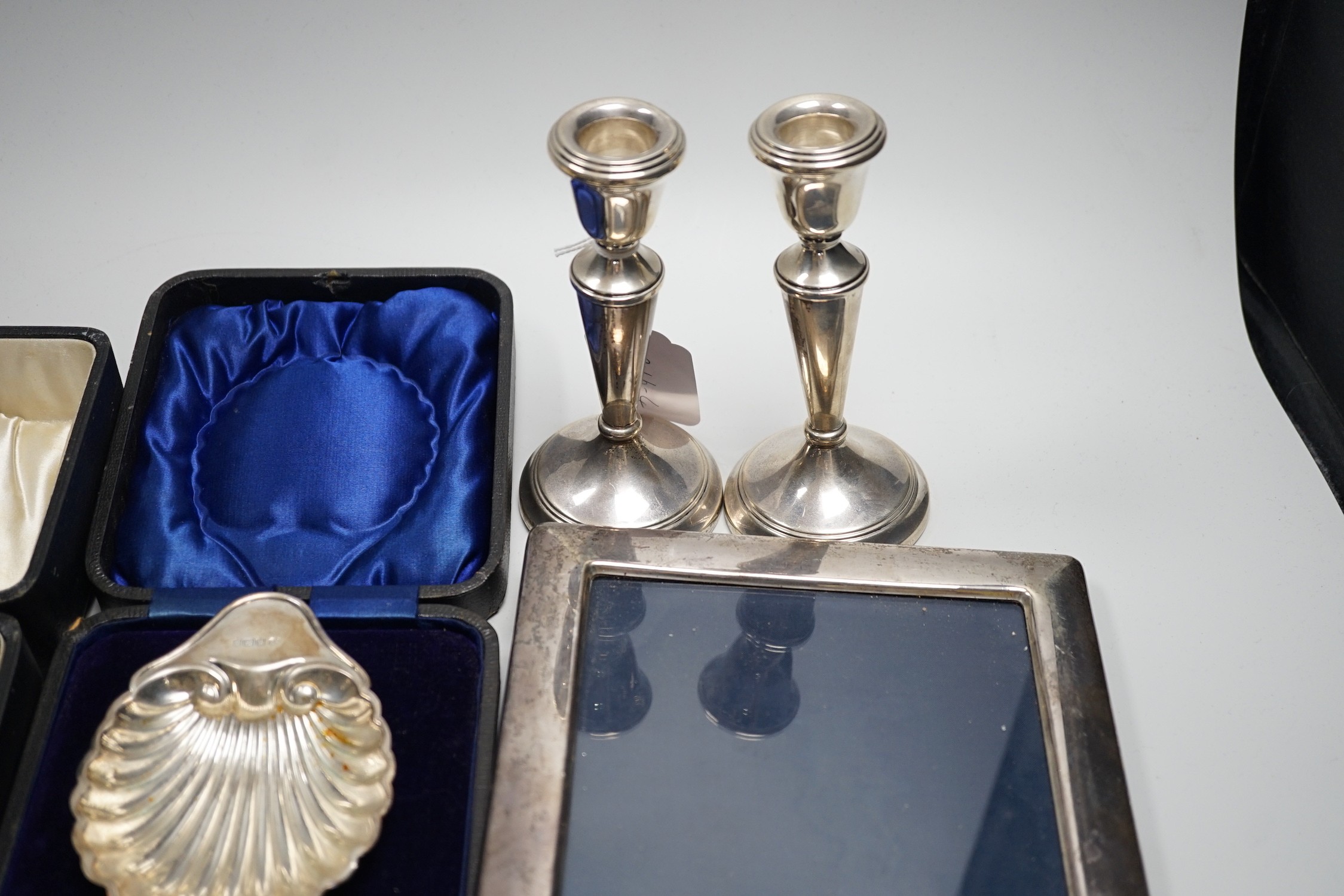 A quantity of mixed silver ware including a pair of modern candlesticks, 15cm, weighted, a cased George V three piece condiment set, cased butter shell and knife, two cased sets of teaspoons, a mounted photograph frame,